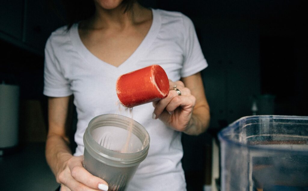 A woman pouring a drink into a blender with powdered ingredients.