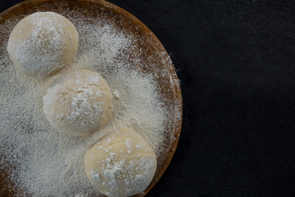 Three dough balls on a plate with powder on it.