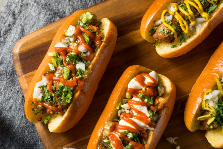 Four hot dogs showcasing food ingredients with different toppings on a wooden cutting board.