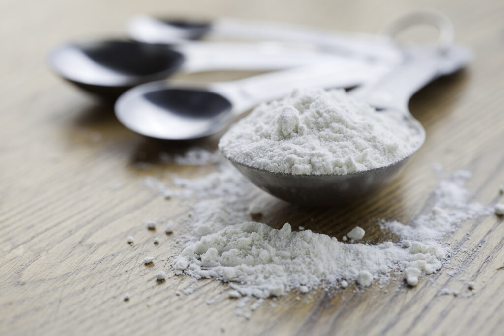 Powdered sugar and measuring spoons on a wooden table.
