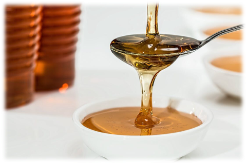 A spoon is pouring honey into a bowl.