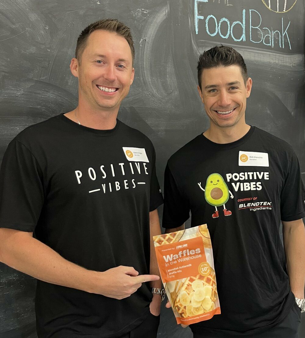Two men standing in front of a blackboard with a positive food bank bag.